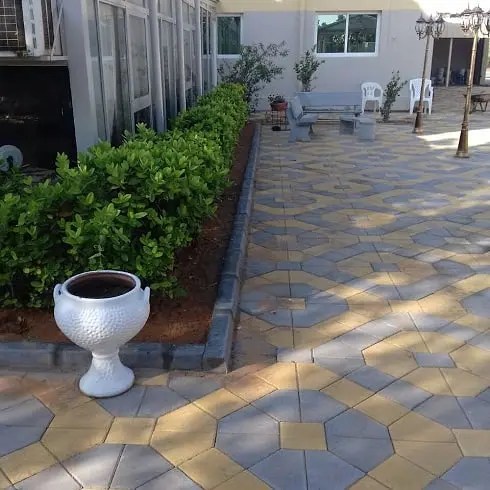 A contemporary landscape design combining grey and yellow interlocking pavers with strips of artificial grass.